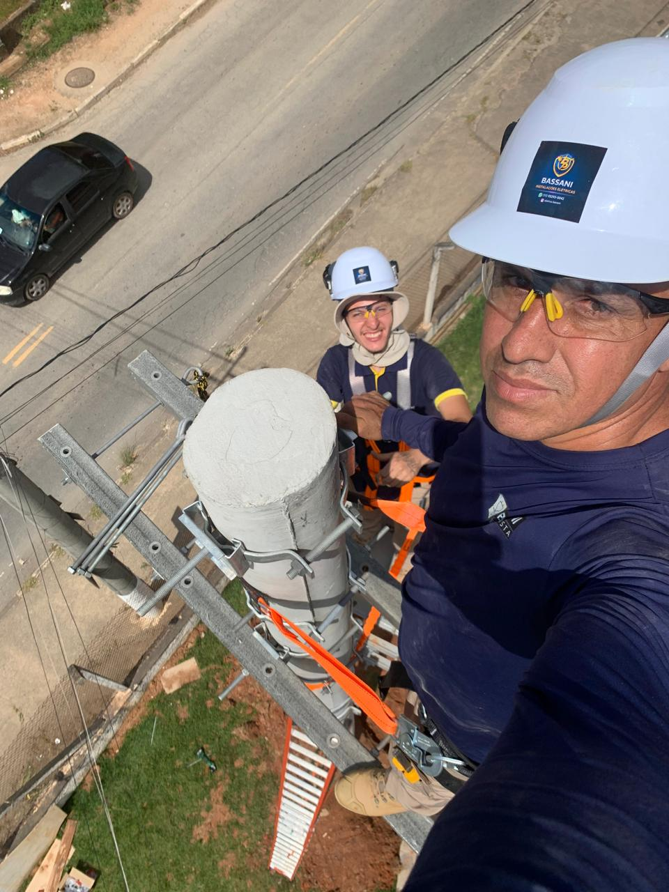 Pedro Bassani e equipe no alto de um poste de concreto, usando capacetes, óculos de proteção e cintos de segurança
